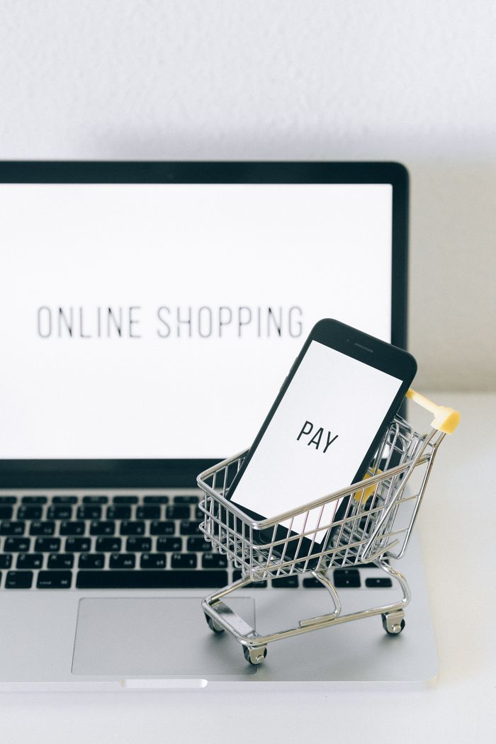 services-04 A smartphone in a miniature cart on a laptop symbolizes online shopping and digital payment.